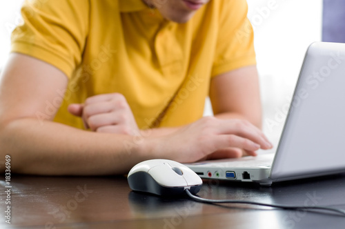 Young man in yellow shirt is sitting in front of his notebook