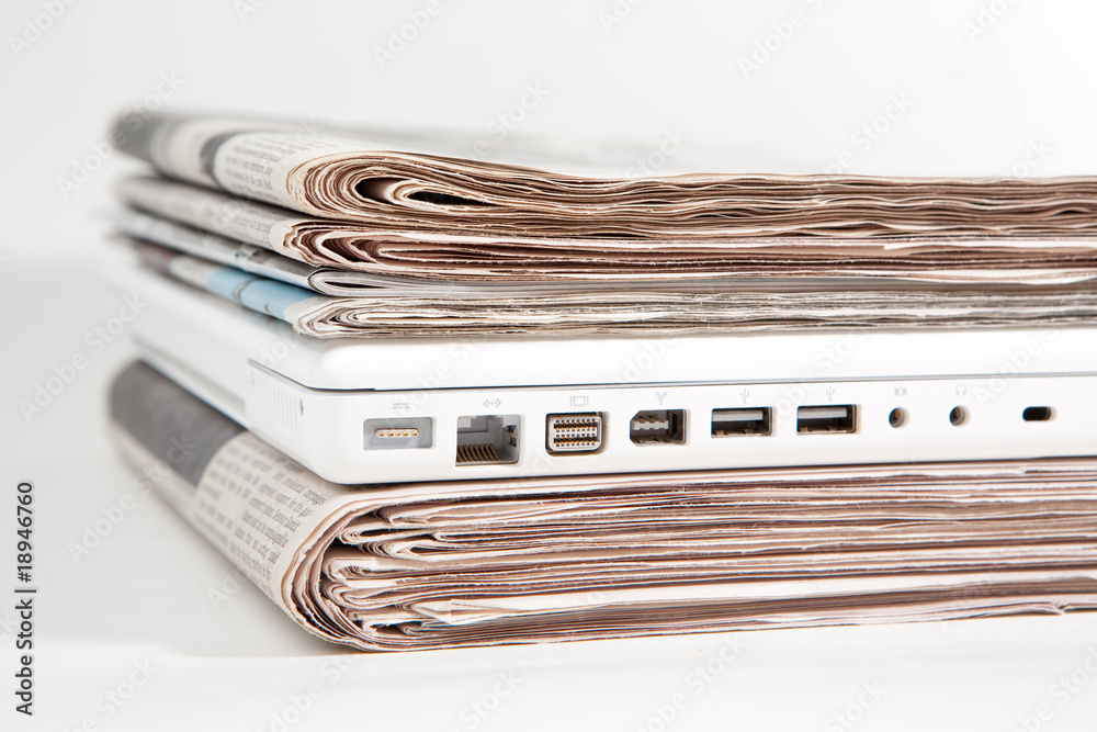 Stapel Zeitungen mit Laptop dazwischen Stapel Zeitungen mit Laptop dazwischen