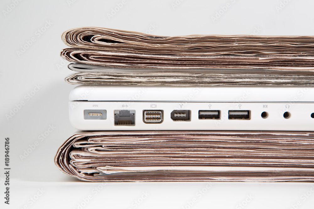 Stapel Zeitungen mit Laptop dazwischen Stapel Zeitungen mit Laptop dazwischen