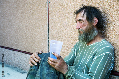 Sad homeless man sitting on at the wall on city street