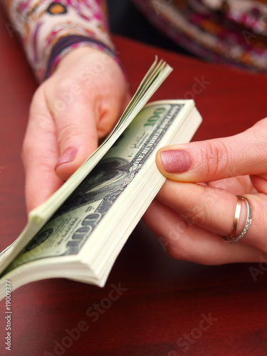 Female hands recalculate a pack of dollars on office table.