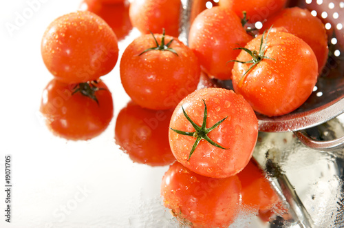 dojrzale czerwone pomidory w sitku, na białym tle, mokre, lustro