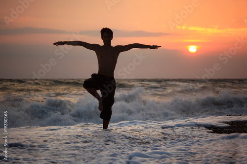 Silhouette guy yoga on sunset wavy beach