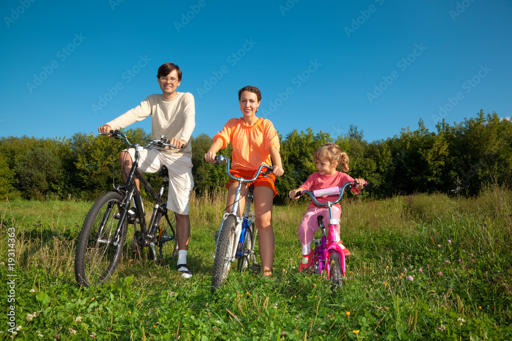 Parents with the daughter on bicycles in park a sunny day.