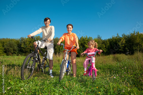 Parents with the daughter on bicycles in park a sunny day.