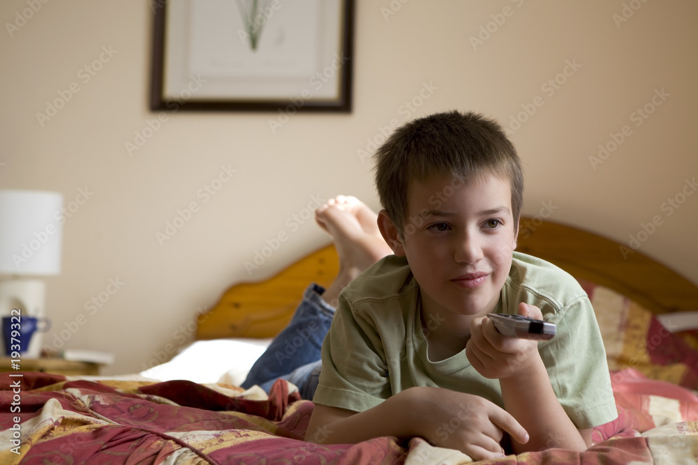 Fototapeta premium boy with a remote control lying on his stomach and watching TV