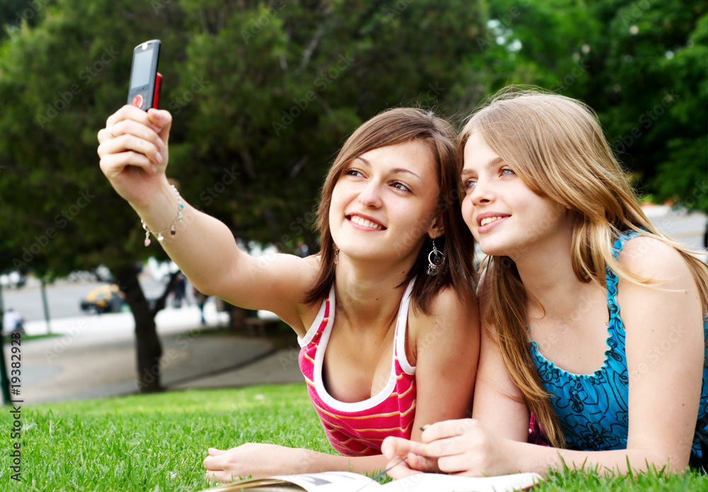 Two girlfriends in park with a mobile phone