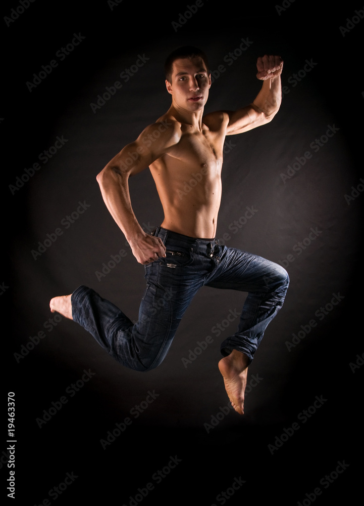 Dramatic light photo of modern acrobat jumping in front of black