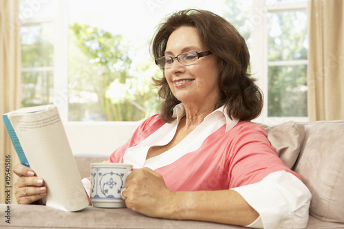 Senior Woman Reading Book With Drink At Home