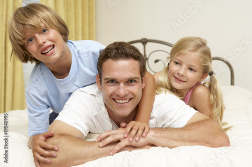 Father And Children Relaxing On Bed At Home