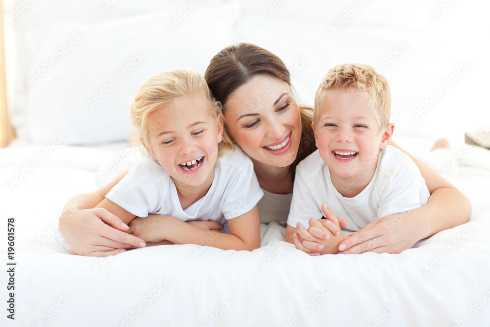 Happy siblings playing with their mother lying on a bed