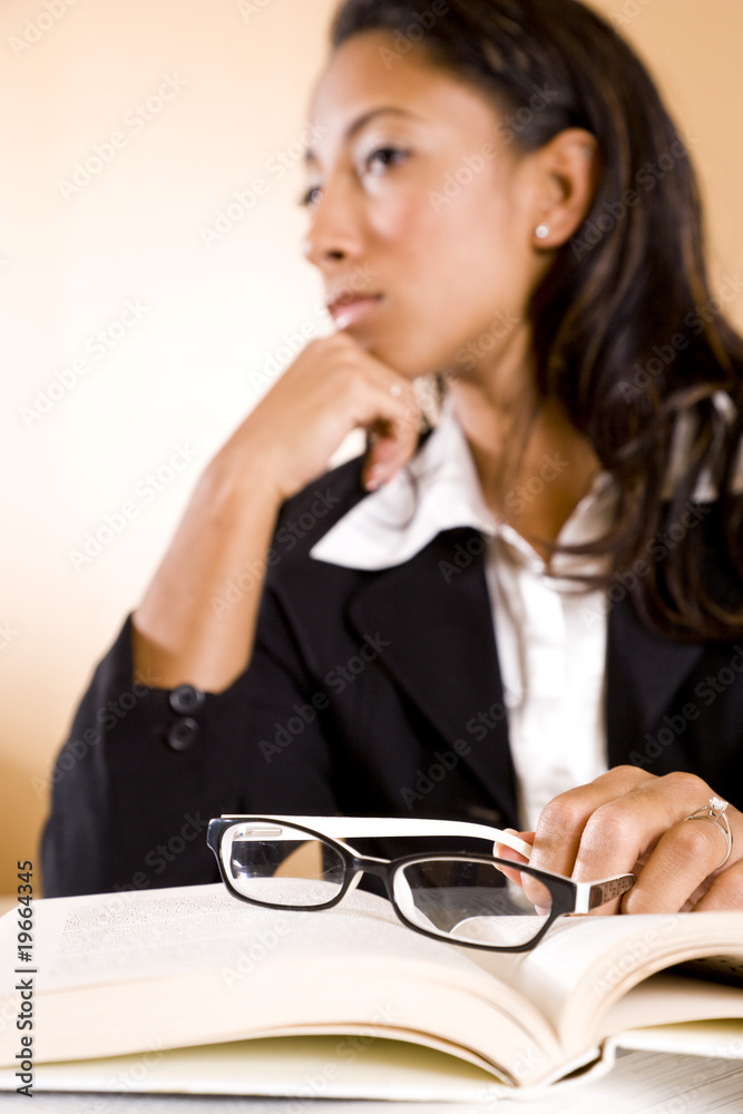 Young woman thinking, focus on eyeglasses on book Young woman thinking, focus on eyeglasses on book