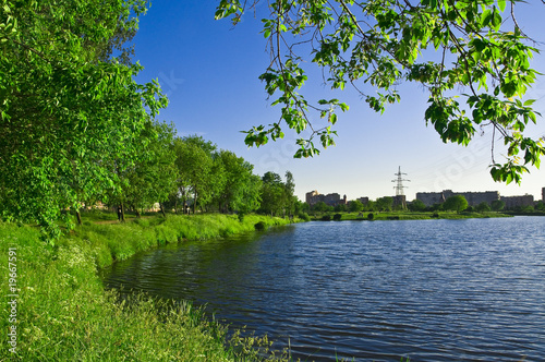 City park beside the lake, green trees in it and blue sky
