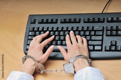 Hands tied with handcuffs on keyboard