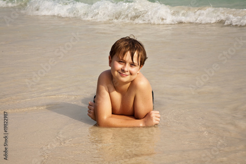 boy is lying at the beach and enjoying the water and the sand
