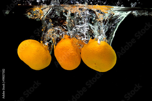 Fresh tangerines dropped into water with bubbles on black
