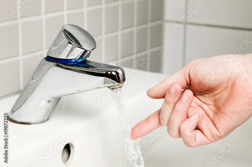 Frauenhand prüft Wassertemperatur am Wasserhahn