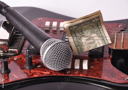 A microphone and dollar lying on a guitar