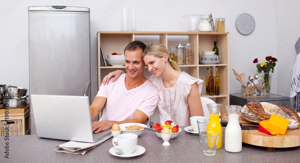 Happy couple using a laptop while having breakfast