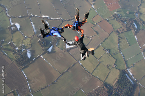 Three skydivers in freefall with snow in the background