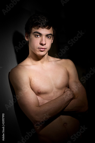 shirtless man with crossed hands leaning against the wall