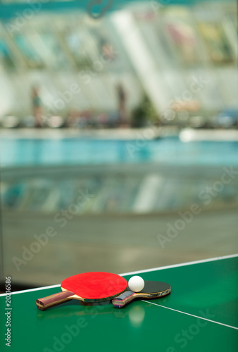 Table tennis rackets and ball swimmig pool in the background