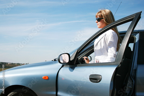 Blonde woman standing near her blue car