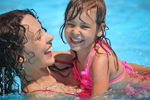 Smiling beautiful woman and little girl bathes in pool