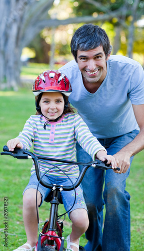Cute little girl learning to ride a bike with her father