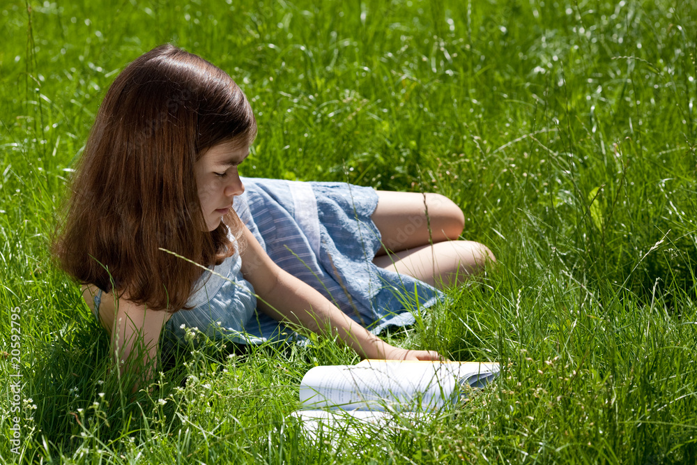 Fototapeta premium Girl reading book lying on green meadow