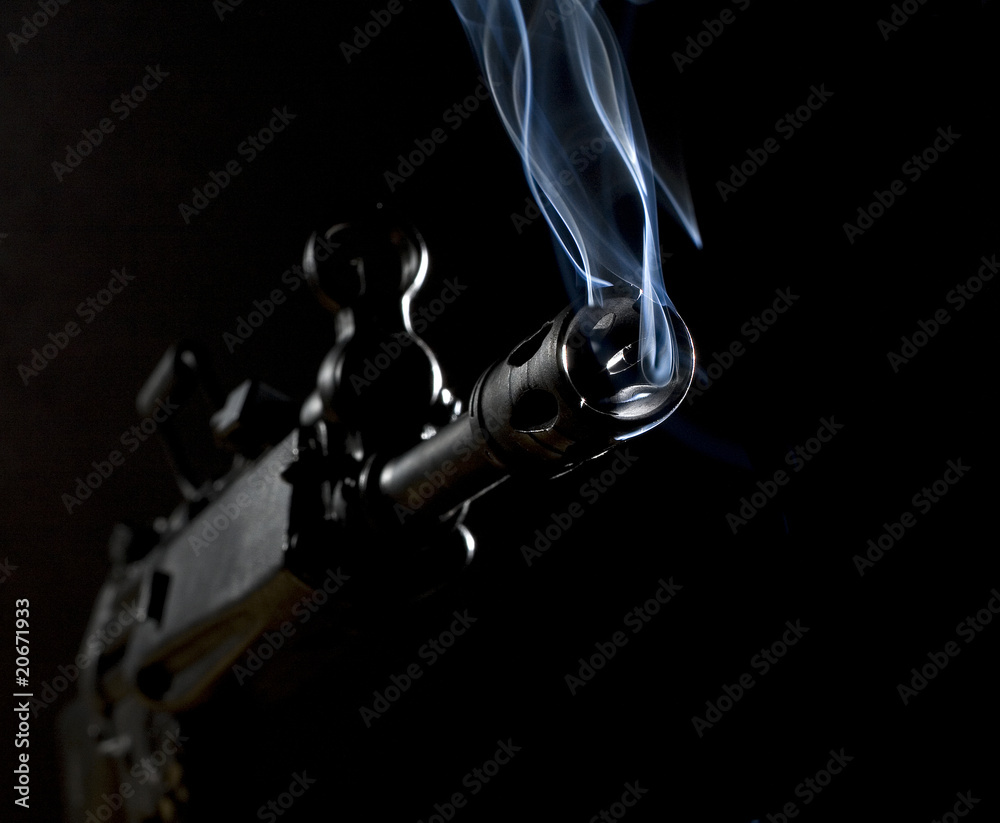 smoke rising from the barrel of an assault rifle on a dark background - obrazy, fototapety, plakaty 