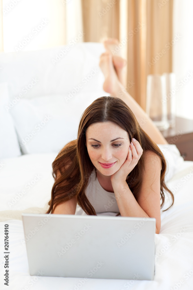 Brunette woman looking at a laptop lying on bed Brunette woman looking at a laptop lying on bed