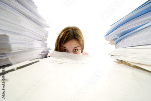jeune femme regardant de derrière un tas de papiers