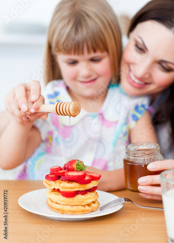 Cute little girl and her mother putting honey on waffles