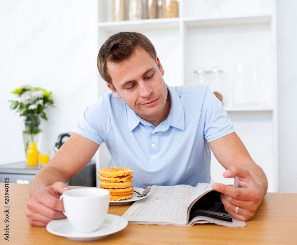 Smiling man reading a newspaper while having breakfast Smiling man reading a newspaper while having breakfast