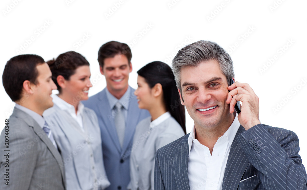 Smiling businessman on phone standing apart from his team Smiling businessman on phone standing apart from his team