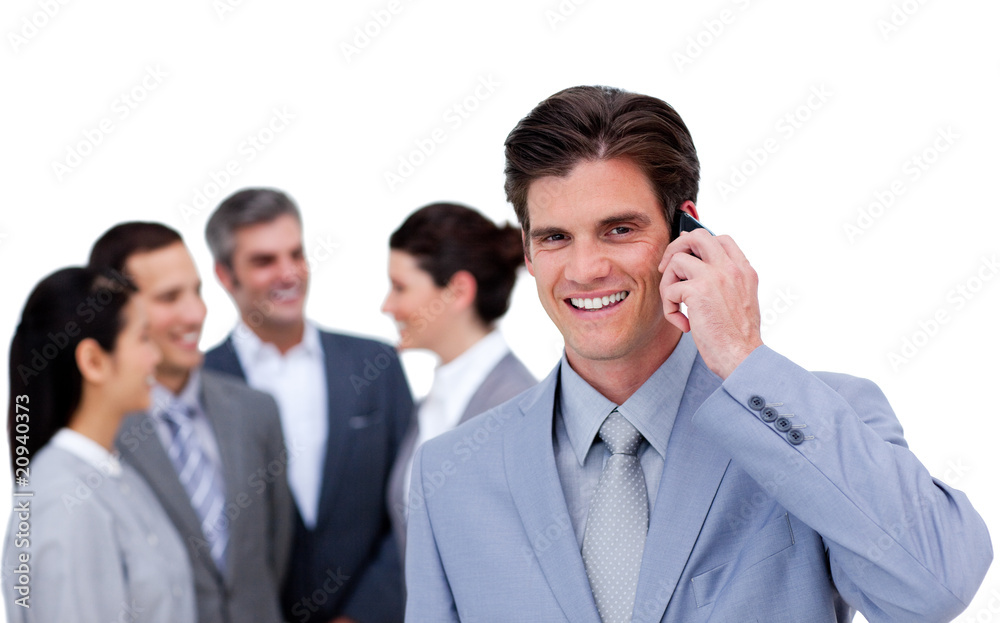 Charismatic businessman on phone standing apart from his team Charismatic businessman on phone standing apart from his team