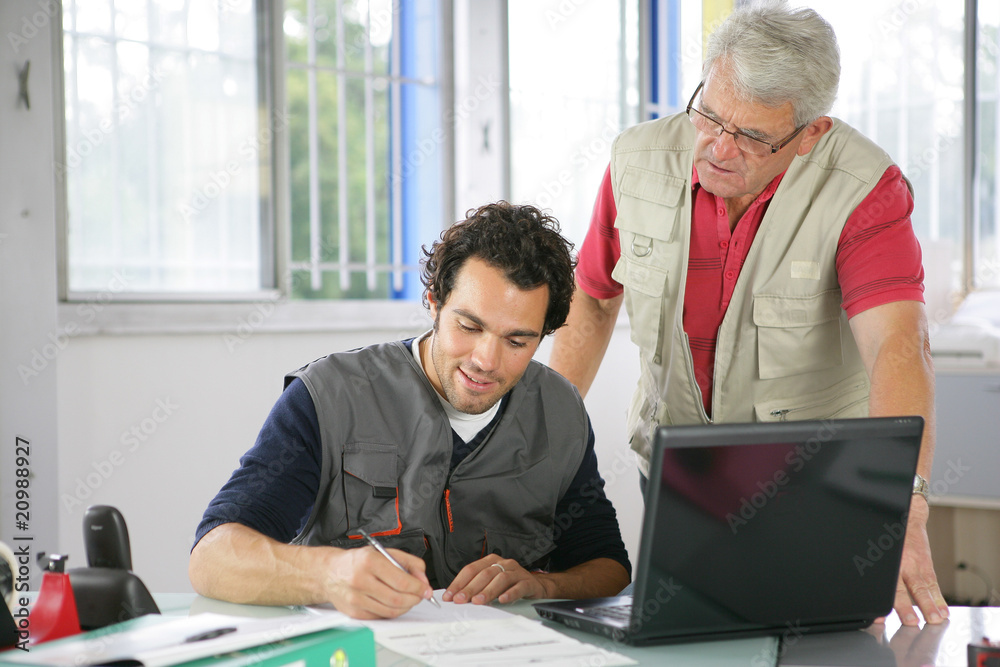 Hommes au bureau devant un ordinateur portable avec documents Hommes au bureau devant un ordinateur portable avec documents