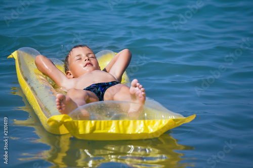 boy in swimming trunks relaxing on an inflatable mattress