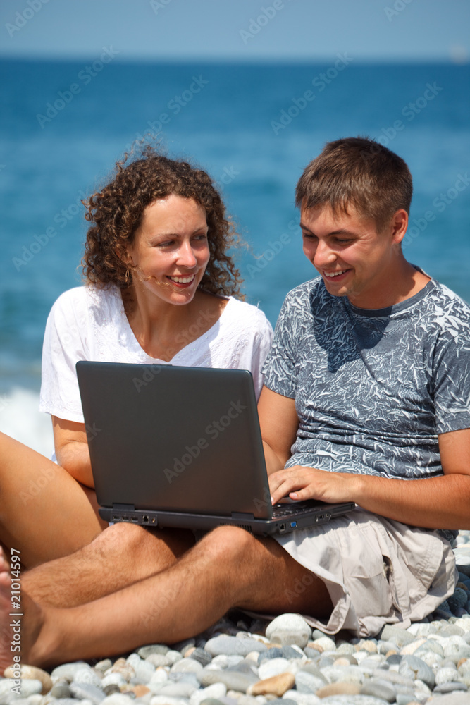Man and girl sitting on seashore. looking at laptop