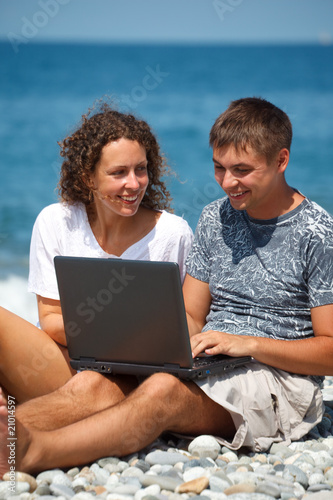 Man and girl sitting on seashore. looking at laptop