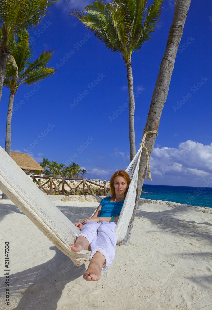 Young woman in hammock on background of palm trees and ocean