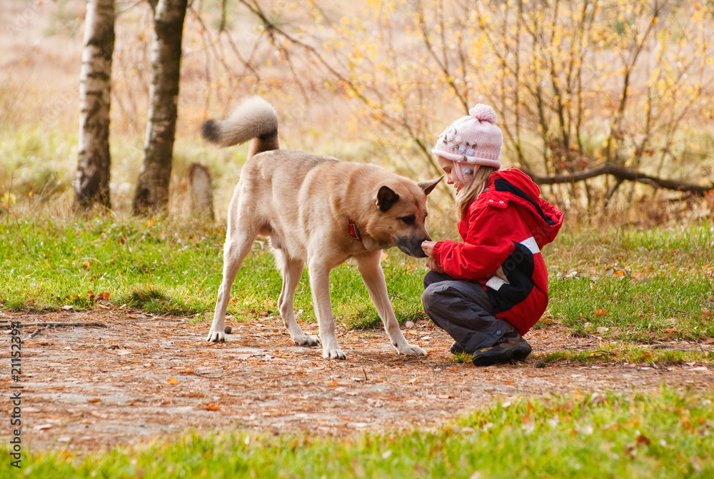 Little girl playing with her dog in autumn forest