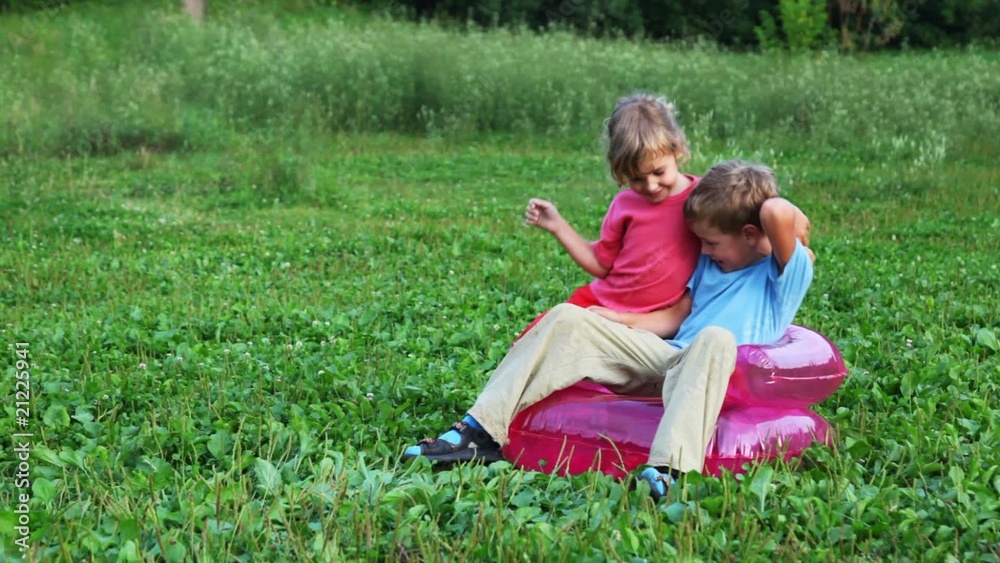 boy and girl sit in inflatable armchair on field and play boy and girl sit in inflatable armchair on field and play