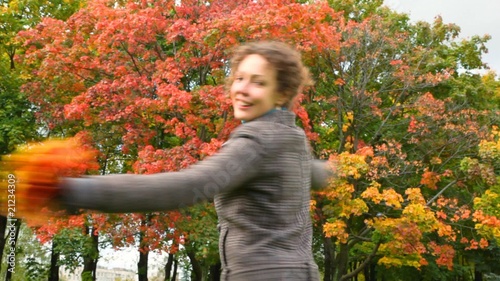 young woman turning around and throwing autumn leaves to camera