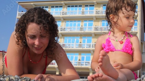 woman and girl fingering stones in beach, hotel in background