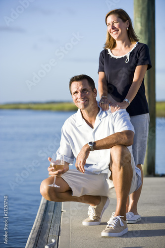 Couple relaxing with drink on dock by water