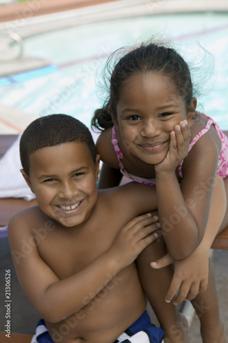 boy (7-9) and girl (5-6) sitting by swimming pool portrait.