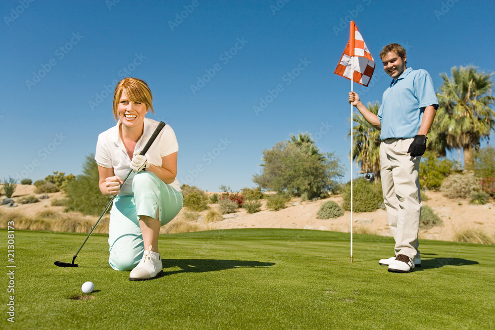 Obraz premium golfing couple watching ball roll towards golf cup