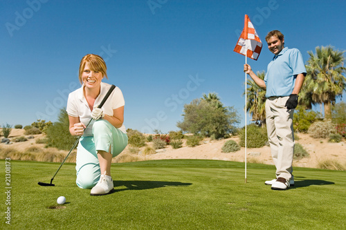golfing couple watching ball roll towards golf cup